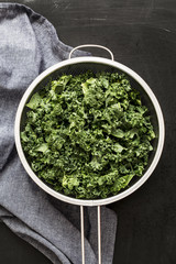Fresh wet kale in a sieve and blue napkin on black chalkboard background captured from above (top view). Preparing food in the kitchen scenery.
