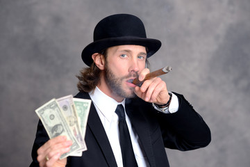 businessman with bowler hat in black suit showing money and smok