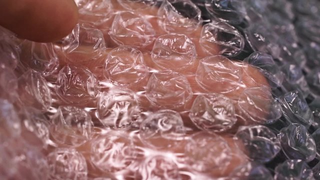 finger bursting air pockets in a sheet of transparent bubble wrap. Macro shot with shallow depth of field