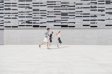 Three young friends in sportswear running in front of a building