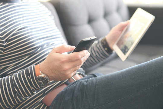 Young Man Sitting Using A Smart Phone And Holding A Tablet , Dressed Casually. Vintage Post Processed. Urban Life Style, Technology, Online, Business, Shopping, Fashion And Job Hunting Concept.