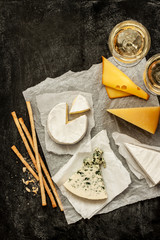 Different kinds of cheeses, white wine and snacks on black chalkboard background captured from...