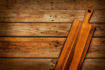 Empty vintage wooden chopping (cutting) board on rustic planked table captured from above (top view). Rural kitchen scenery. Background layout with free text space.