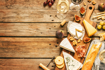 Different kinds of cheeses, wine, baguettes, fruits and snacks on rustic wooden table from above....