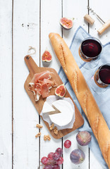 Camembert, prosciutto (jambon italien), baguette, deux verres de vin rouge, figues et raisins. Table en bois blanc comme toile de fond. Paysage de pique-nique français romantique capturé d& 39 en haut (vue de dessus).
