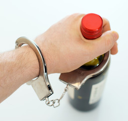 Hand handcuffed to bottle of wine. Alcoholism concept.