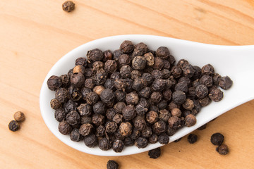 Spoonful of aromatic and spicy black pepper corns on wooden surface