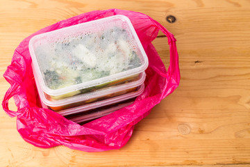 Convenient but unhealthy disposable plastic lunch boxes with take away meal in plastic bag on wooden table