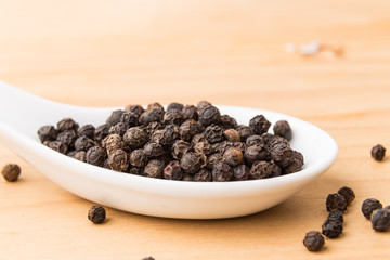 Spoonful of aromatic and spicy black pepper corns on wooden surface