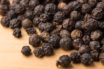 Heaps of aromatic black pepper corns on wooden surface