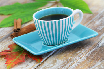 Black coffee in vintage stripy cup and cinnamon sticks on rustic wooden surface
