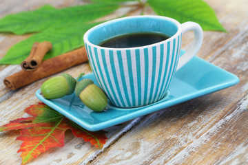 Black coffee in vintage stripy cup, acorns and cinnamon sticks on rustic wooden surface
