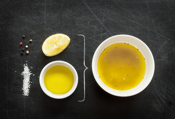Lemon vinaigrette dressing - recipe ingredients on black chalkboard background from above. Lemon, olive oil, salt and pepper. Layout with free text space.
