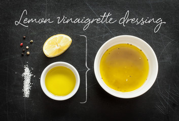 Lemon vinaigrette dressing - recipe ingredients on black chalkboard background from above. Lemon, olive oil, salt and pepper. Kitchen poster layout.