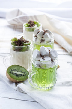Jelly with kiwi fruit with marshmallows and grated chocolate in glass, sliced kiwi on white wooden table