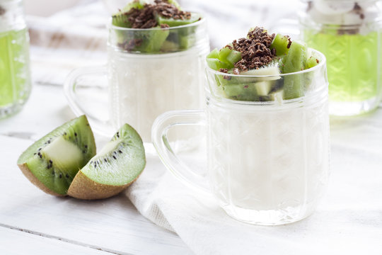 Vanilla panna cotta with kiwi and grated chocolate in glass, sliced kiwi on white wooden table