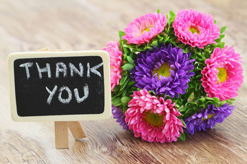 Thank you written on mini blackboard and colorful daisy bouquet

