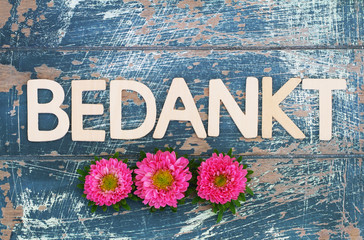 Bedankt (thank you in Dutch) written with wooden letters on rustic surface and pink daisies
