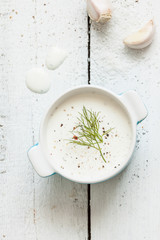 Creamy garlic dip in a bowl on white rustic wooden background from above.