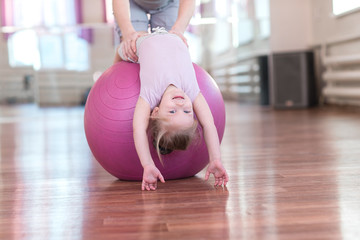 Mom is doing exercises gymnastics coach with a daughter in the gym.