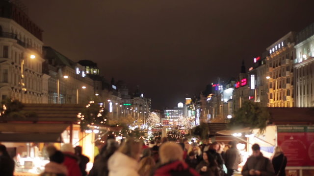 Christmas market fair in Prague street at night full of light. Pedestrians walk at Christmas market at night passing by illuminated Christmas fair tent kiosks. Christmas in Europe