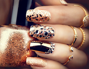 Heldere manicure in gouden vakantiestijl met edelstenen en glitters. Trendy accessoires