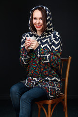 Attractive brunette girl in a sweater with a hood holds a mug of