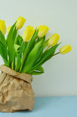 yellow tulips in brown paper bag on the table with wall background
