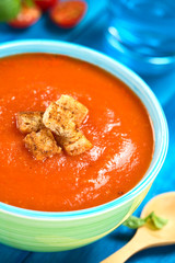 Fresh homemade tomato soup with wholegrain croutons on top served in colorful bowl on blue wood (Selective Focus, Focus on the croutons in the front)