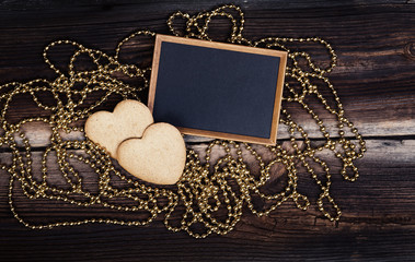 Two Heart Shaped Cookies, Blackboard And Golden Beads On Very Old Wooden Board. Happy Valentines Day. Romantic Composition.