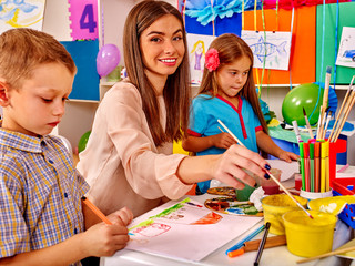 Children with female teacher painting on paper by paint and pencils  in  kindergarten .  - 100913494