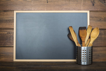 Pizarra vacía con espacio para texto sobre fondo de madera y utensilios de cocina