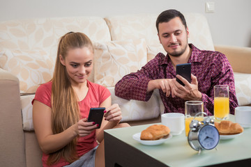 Cute young couple having breakfast and looking at mobile phone 