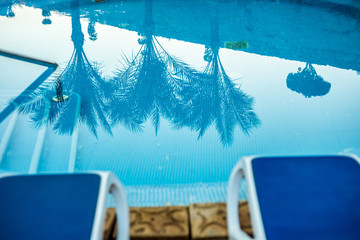 Closeup sunloungers and swimming pool with reflected palms in water 