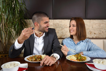 Fototapeta na wymiar Young couple at the restaurant eating Chinese food with chopsticks