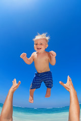 Fototapeta na wymiar Family swimming fun on white sand sea beach and blue sky - father hands tossing up baby boy into mid air and catching. Child outdoor activity, active lifestyle on summer vacation in tropical island.