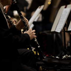 Hands of man playing the clarinet in the orchestra in dark colors