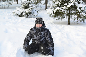 Fototapeta na wymiar Teen boy sitting on snow in the winter forest
