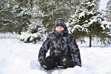 Fototapeta na wymiar Teen boy sitting on snow in the winter forest