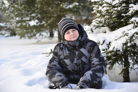 Teen boy sitting on   snow in the winter forest