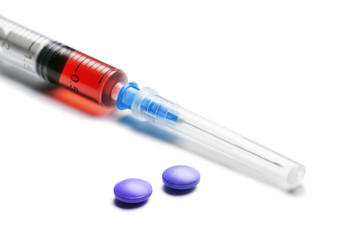 Syringe filled with red liquid and blue pills on white background