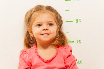 Little girl measuring height against wall in room