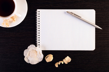 cup of hot coffee, notebook, pen, flowers on the wooden background. Place for text. Square image.