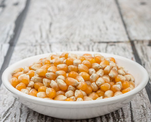 Raw popcorn in white bowl over wooden background