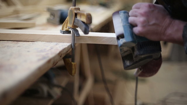 A carpenter polishes a piece of wood clamped in a vise belt using sander machine
