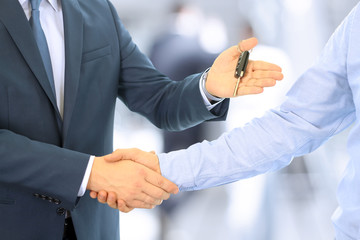 Car salesman handing over the keys for a new car to a young busi