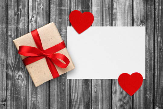 Blank paper with gift box and red hearts on black and white wooden background