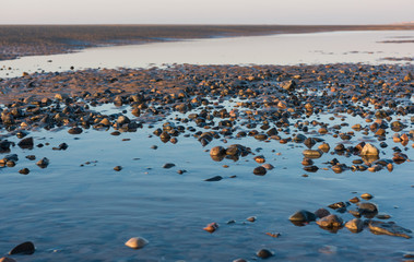 Beautiful sunny winters day on a british beach, with sand ripples, beach stones and the sky reflecting in a water pool.