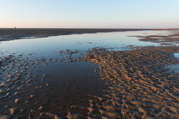 Beautiful sunny winters day on a british beach, with sand ripples and the sky reflecting in a water pool.
