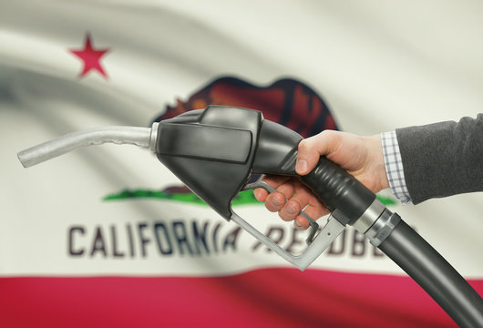 Fuel pump nozzle in hand with USA states flags on background - California